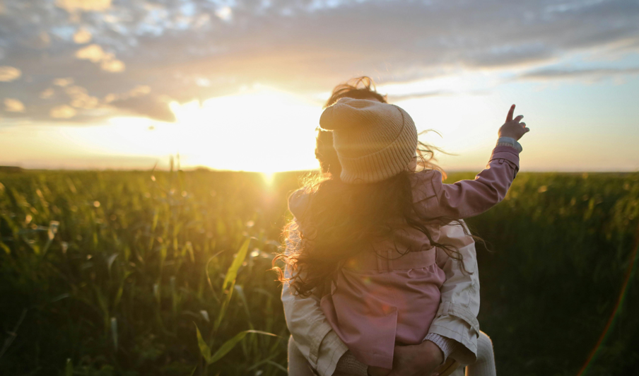 Mutter und Kind genießen den Sonnenuntergang auf einem Feld und gestalten mit einem nachhaltigen Lebensstil aktiv die Zukunft.