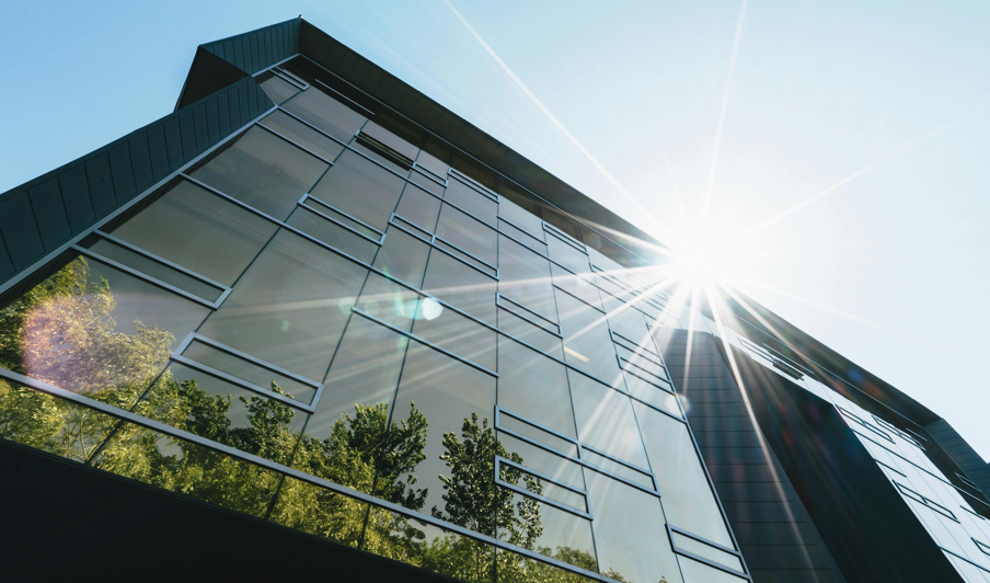 Modernes Bürogebäude mit Sonnenreflexionen auf der Glasfassade; Solarstrom ist ein wichtiger Pfeiler der Energiegemeinschaft.